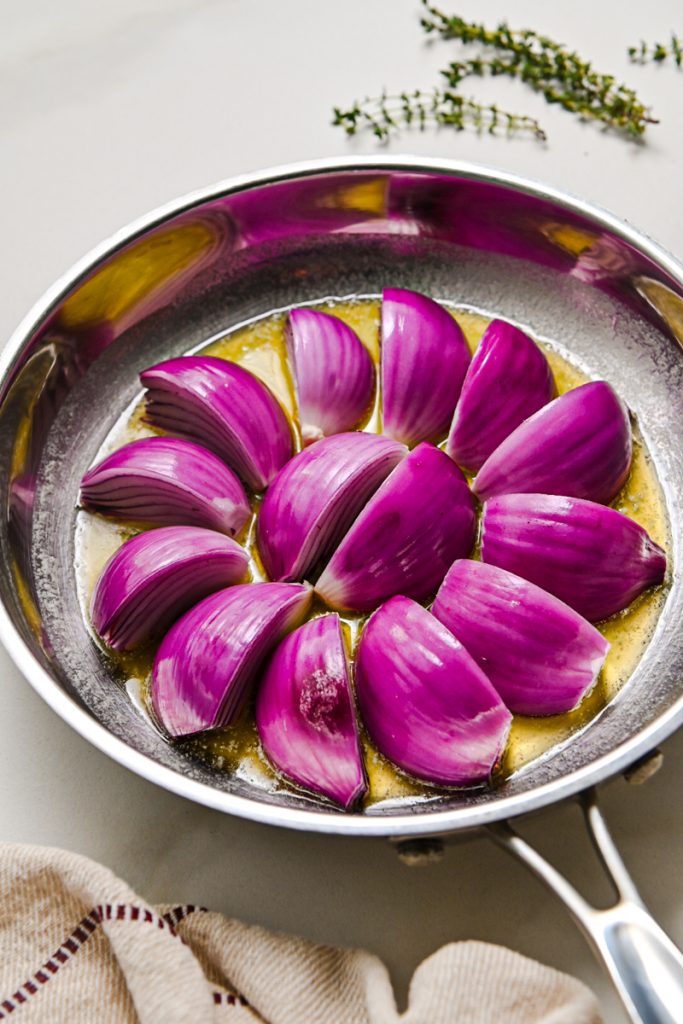 Red onions wedges in a skillet to sear.