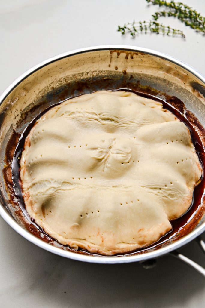 Puff pastry added over top of the sautéed red onions in a skillet.