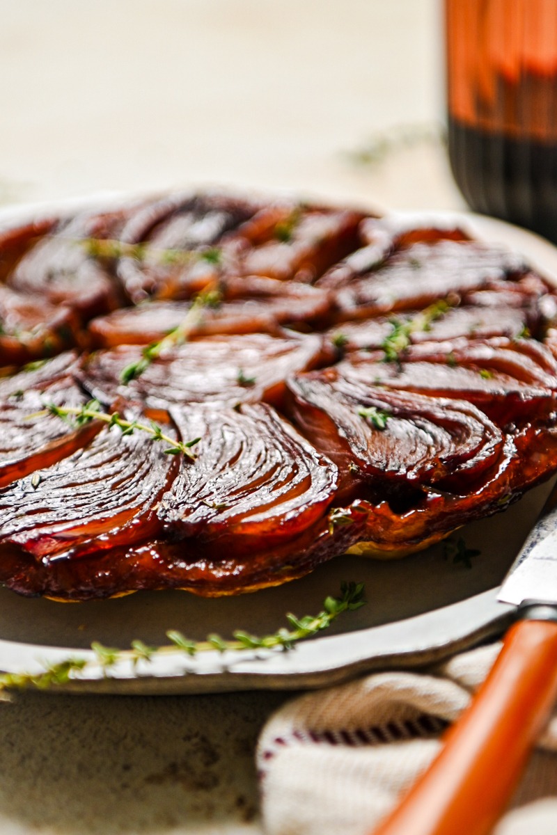 Side view of a red wine onion tarte tartin on a serving platter with fresh thyme on top.