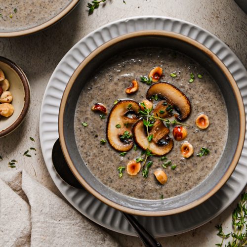 Overhead shot of a bowl of creamy mushroom soup topped with sliced mushrooms and fresh thyme.