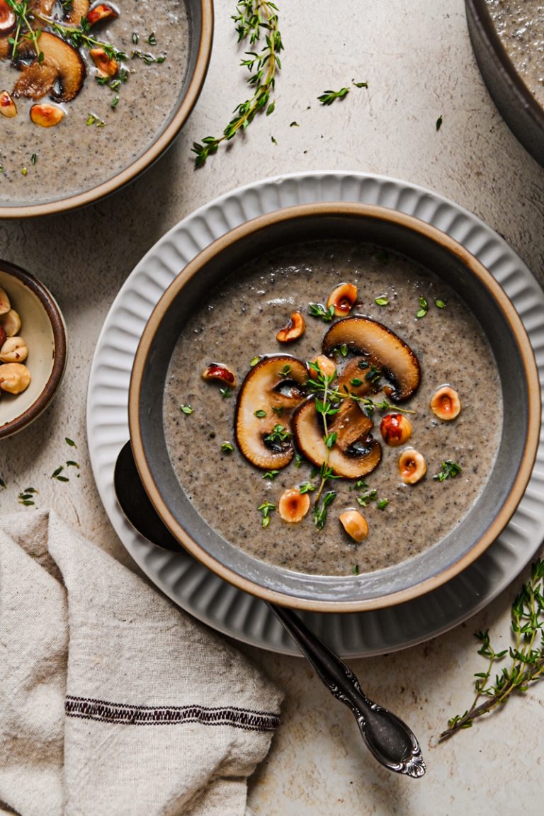 Overhead shot of a bowl of creamy mushroom soup topped with sliced mushrooms and fresh thyme.