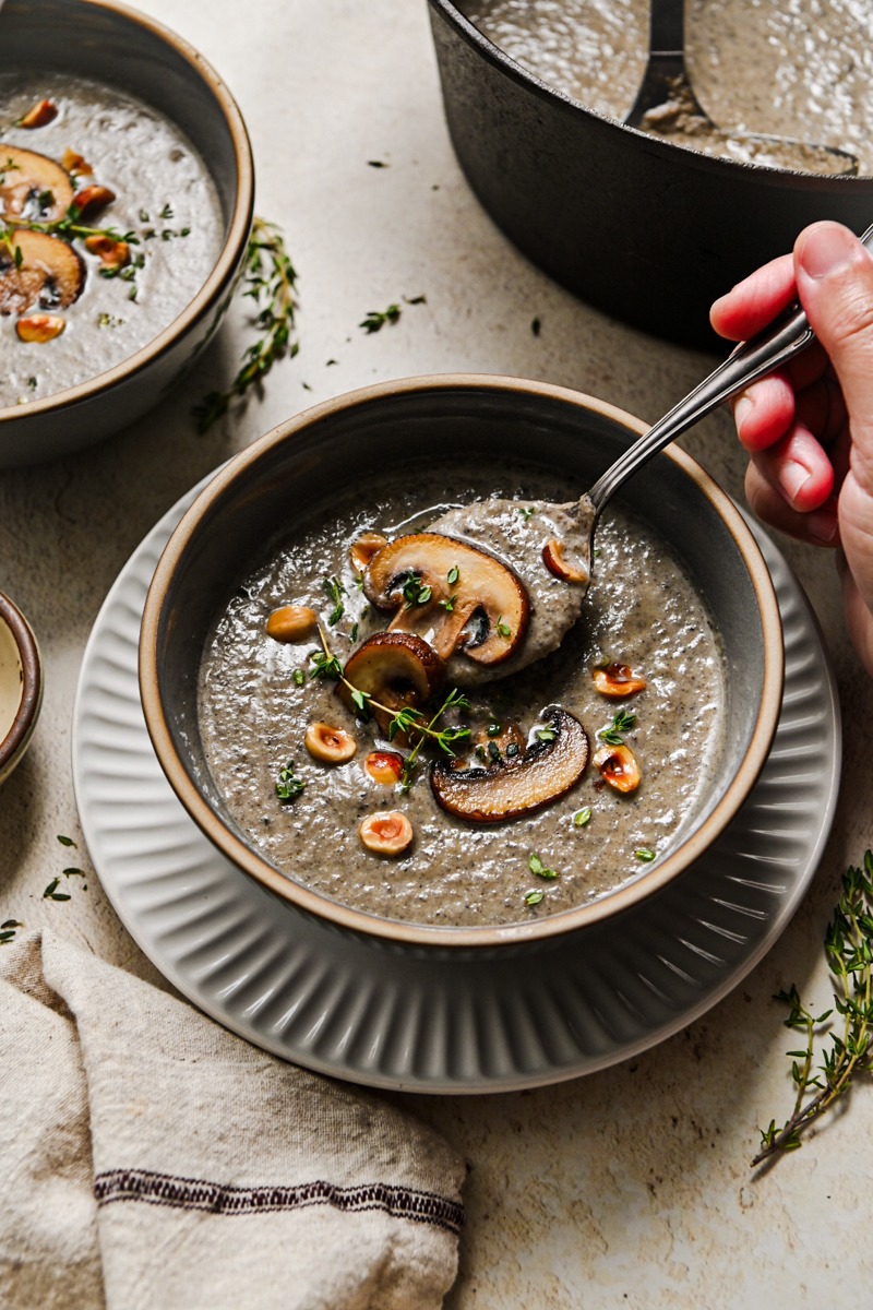 Hand holding a spoon, taking a bite of soup from the bowl of mushroom soup.