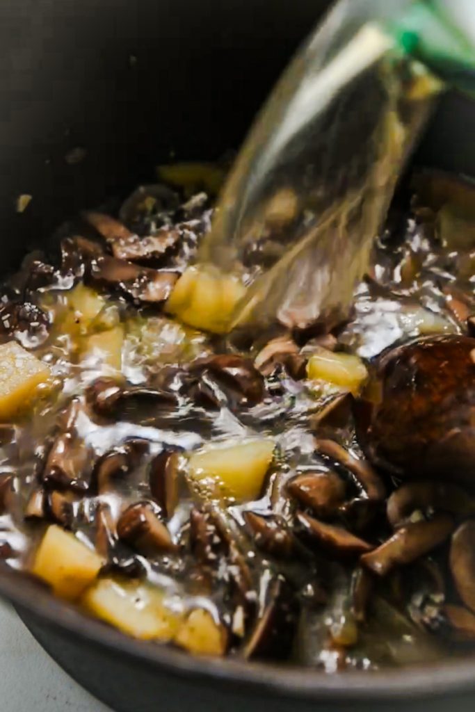 Broth being poured into the pot with onions, mushrooms and potatoes in it.