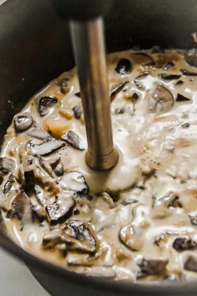 Using an immersion blender to blend the mushrooms soup in a pot.