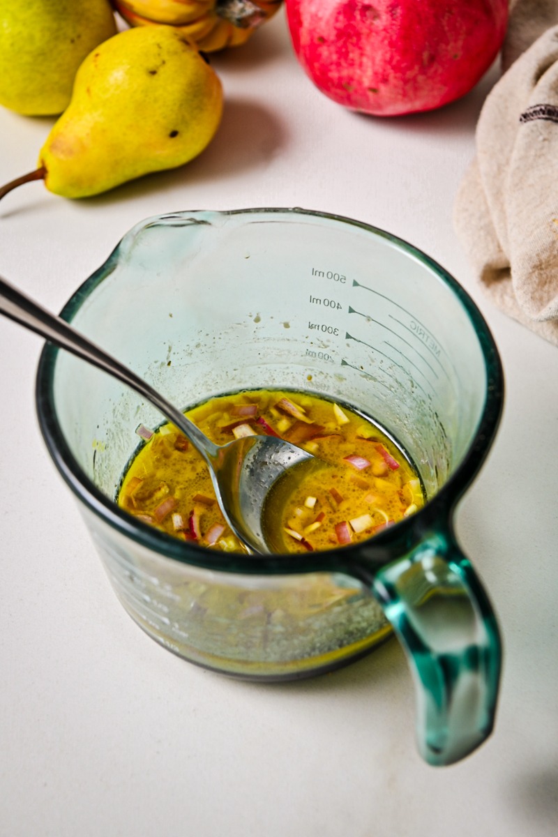 Maple dijon dressing being mixed together in a glass measuring cup.