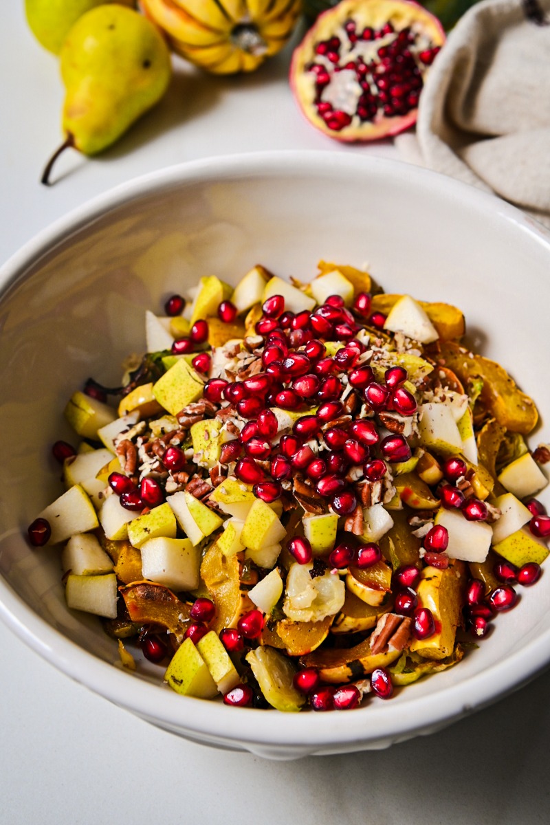 Pomegranate and pears added to the vegetables in a mixing bowl.