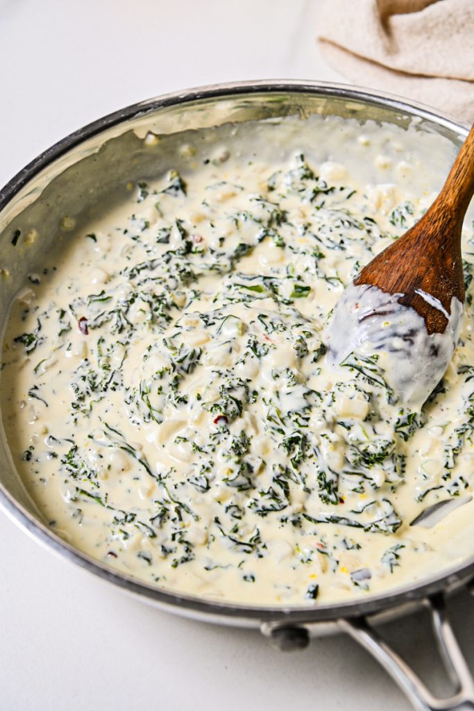 Heavy cream added to the kale mixture in a skillet.