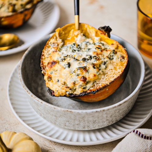 Roasted acorn squash stuffed with kale and goat cheese filling served in a bowl.