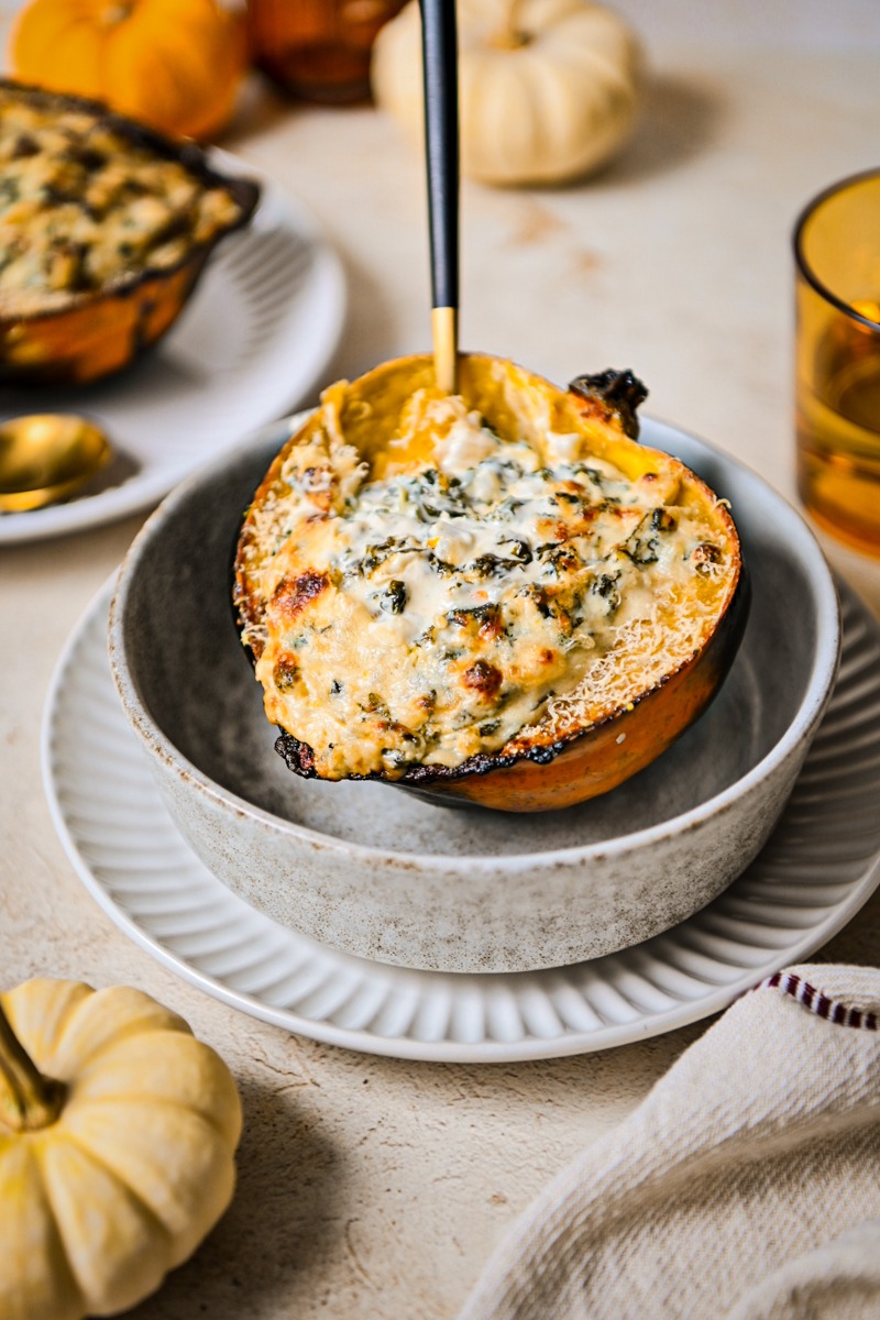 Roasted acorn squash stuffed with kale and goat cheese filling served in a bowl.