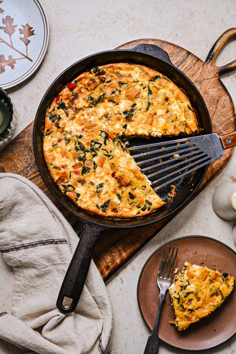 Overhead shot of butternut squash feta skillet quiche in a cast iron skillet with a piece missing.