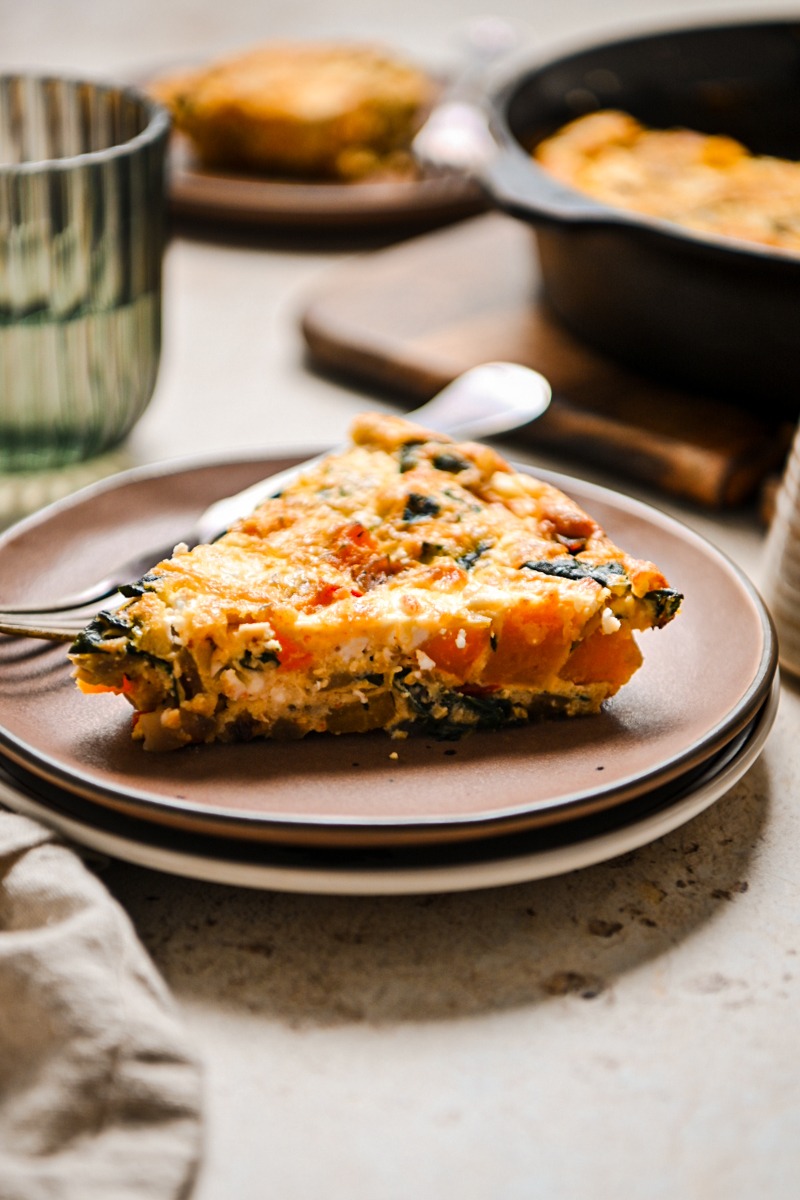 Slice of butternut squash quiche on a plate with a fork.