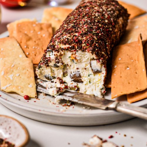 Side view of an olive and feta cheese log with a slice off the end served with crackers.