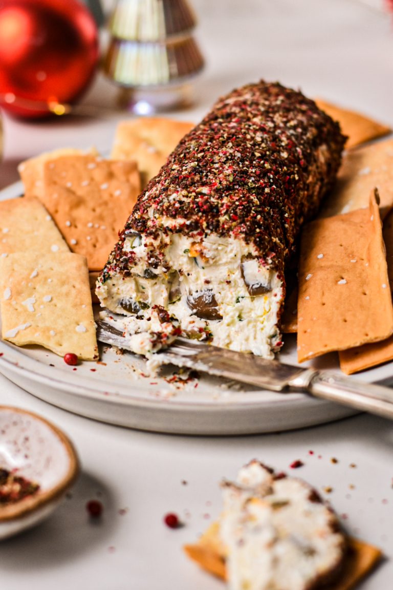 Side view of an olive and feta cheese log with a slice off the end served with crackers.