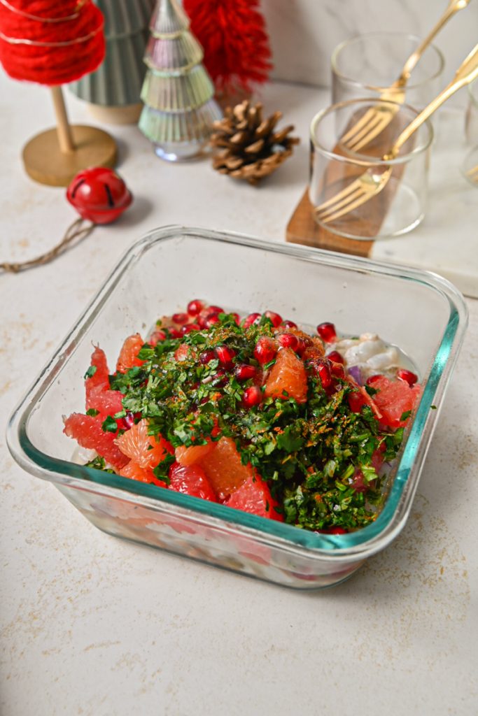Citrus, pomegranate, and cilantro added to the shrimp in a glass container.