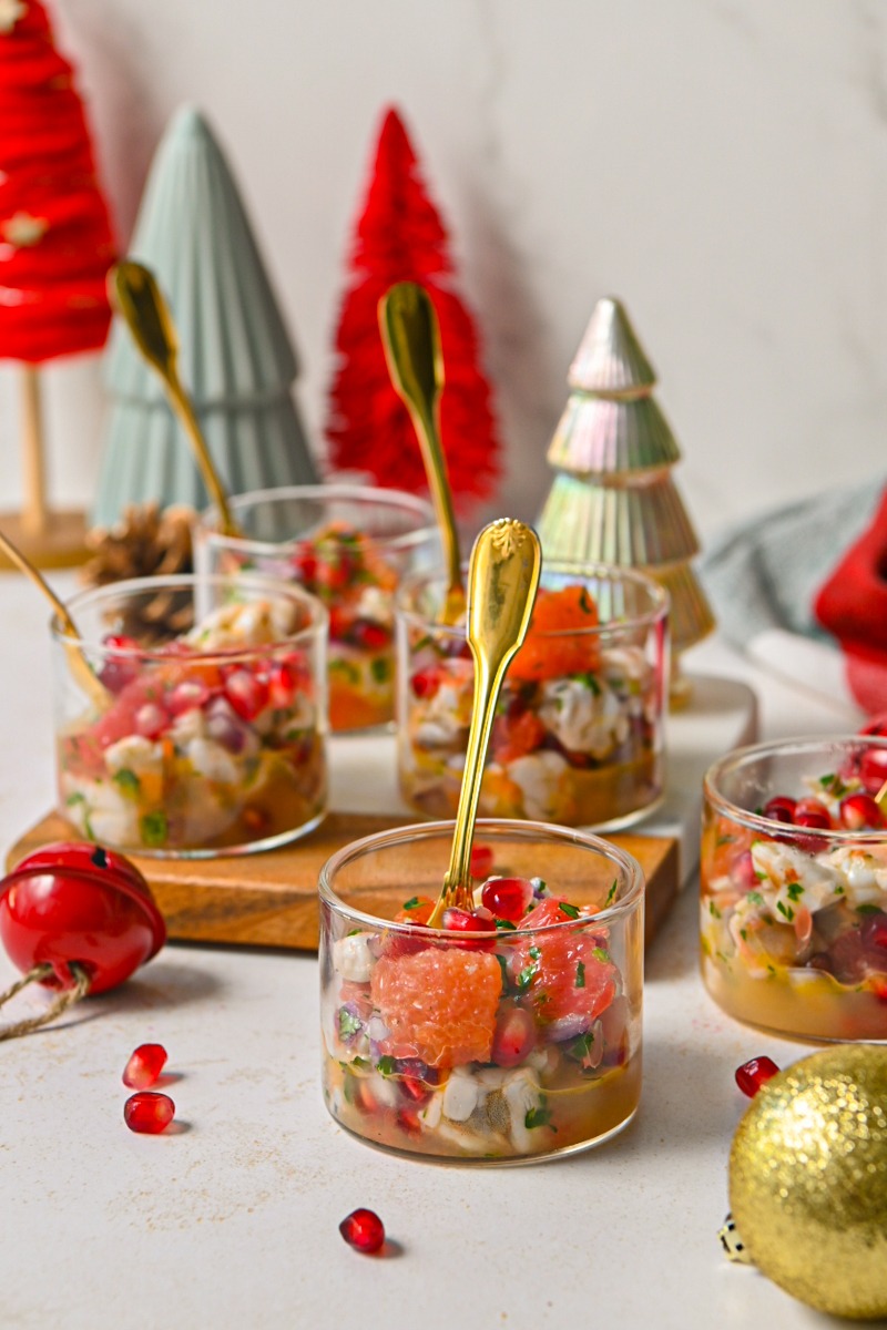 Side view of citrus pomegranate shrimp ceviche in small glasses with spoons around holiday decorations.