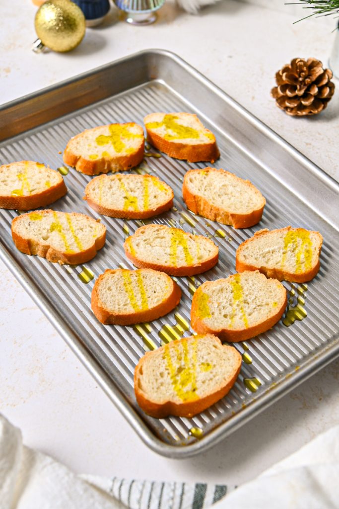 Sliced baguette pieces on a sheet pan drizzled with olive oil.