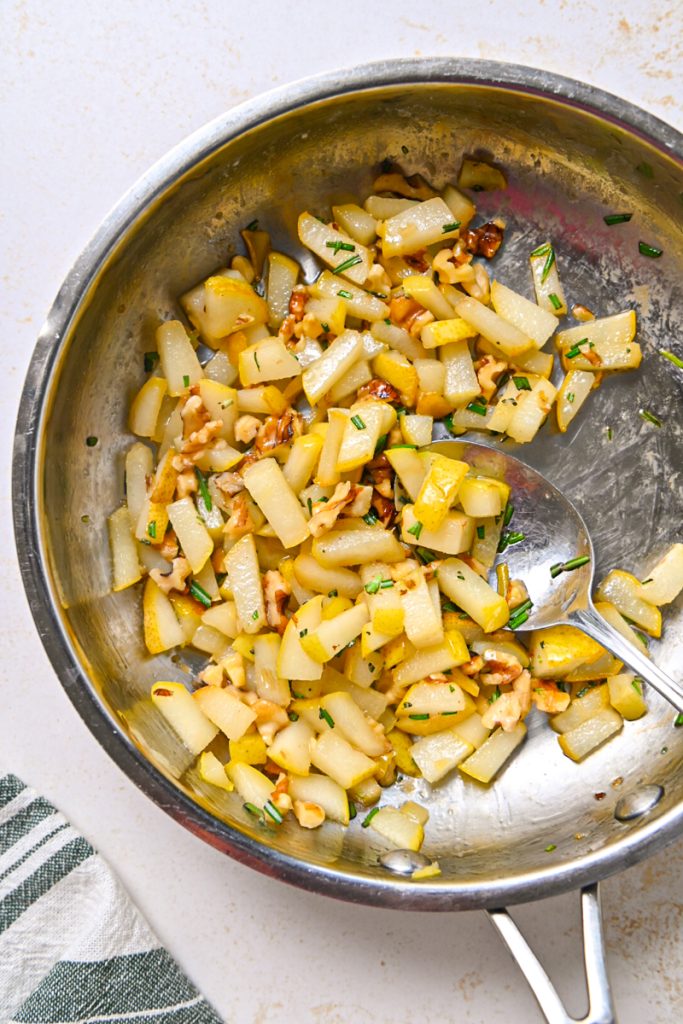 Walnuts and rosemary added to the pears in a skillet.