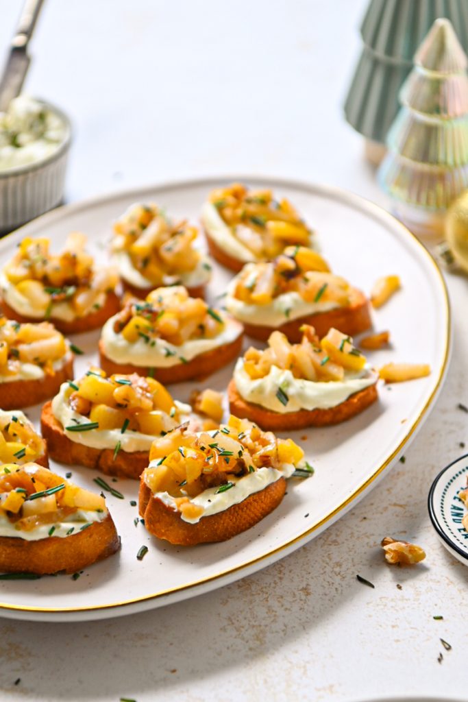 Side view of whipped gorgonzola crostini with sautéed pears on a serving platter.