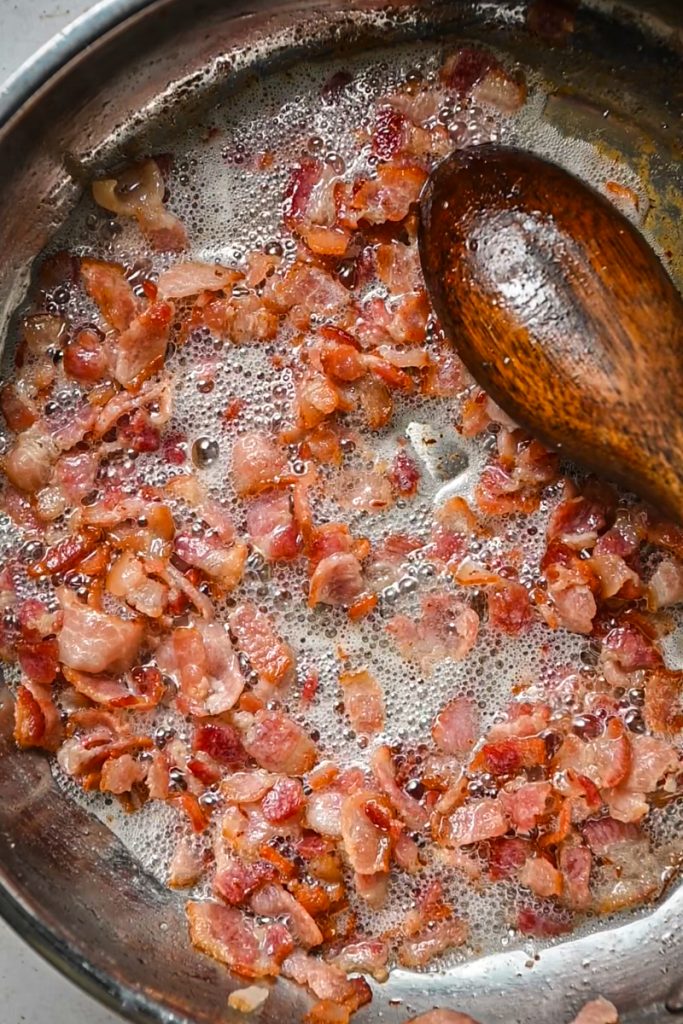 Pieces of bacon crisping up in a skillet.