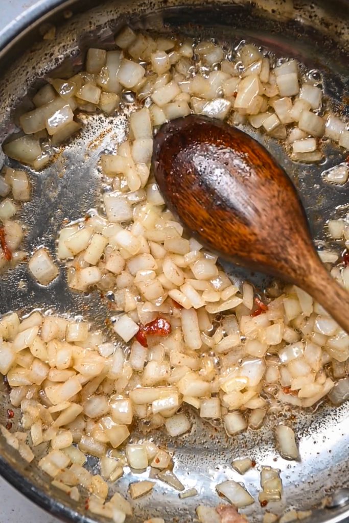 Onions being sauteed in bacon fat in a skillet.