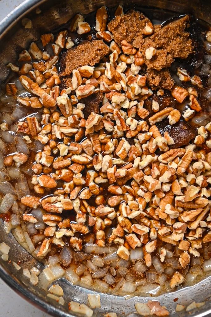 Pecans, brown sugar, and maple syrup added to the onions and bacon in a skillet.