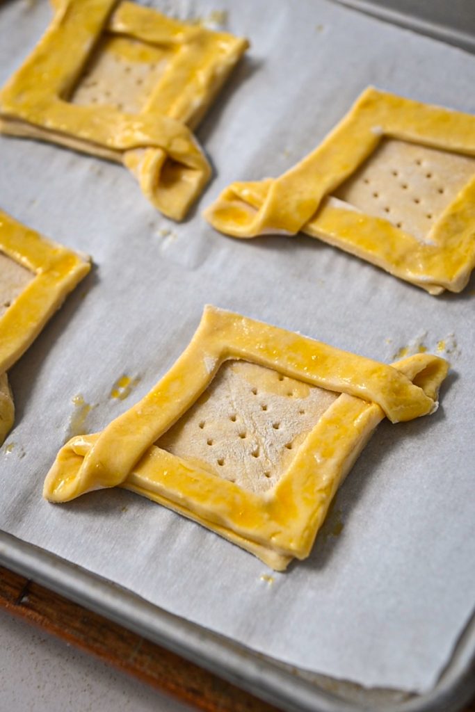 Egg wash on top of the puff pastry squares with fork marks in the center.