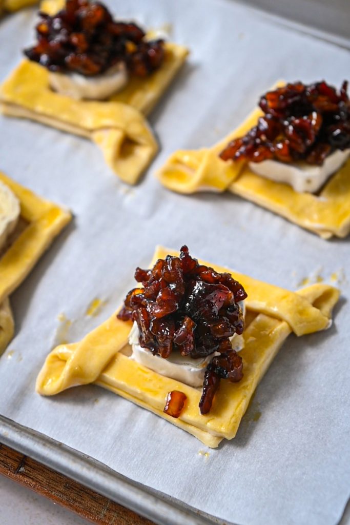 Brie and bacon jam on top of assembled puff pastry squares before baking.