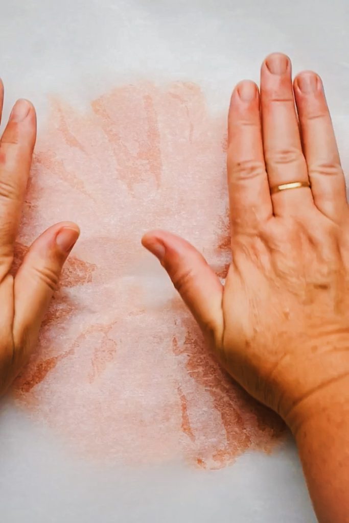 Hands covering the circle of smoked salmon with another piece of parchment paper.