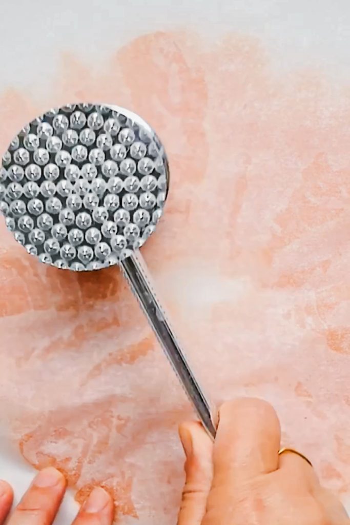 Using a meat pounder to pound the smoked salmon into thin pieces.