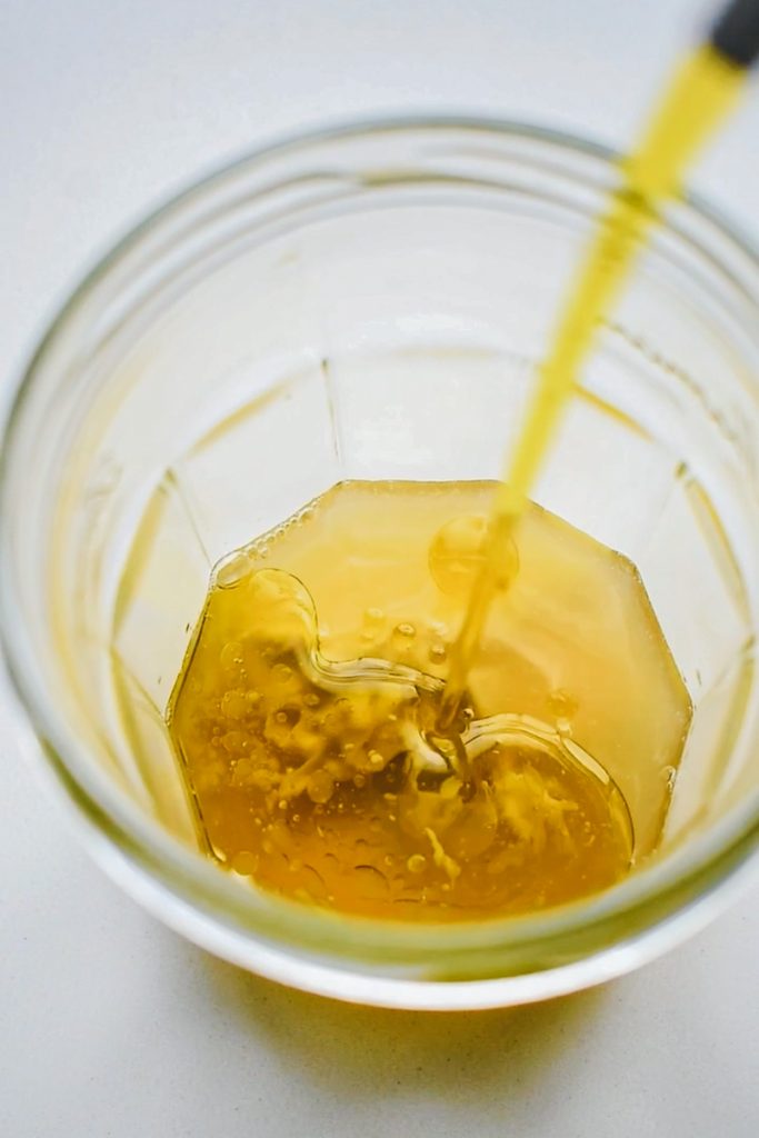 Pouring olive oil into a jar with lemon and dijon mustard in it.